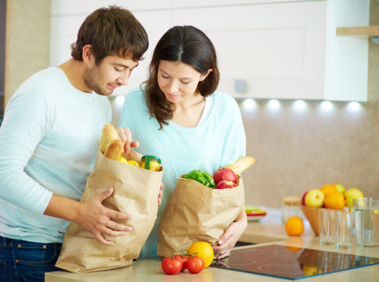 Pretty female and her husband looking at products in paperbags in the kitchen